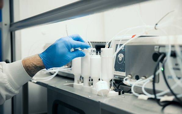 Technician wearing a blue glove adjusts laboratory equipment used for quality control testing of recycled plastic materials in a clean lab environment.